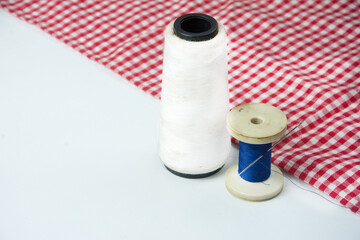 spool of thread and needle on a red and white tablecloth