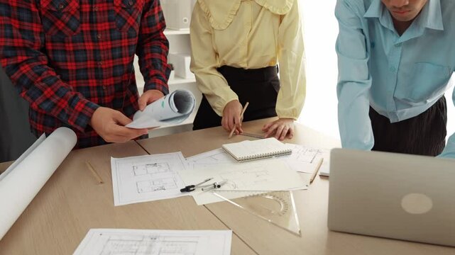 Professional engineer team discussion about house design on meeting table with architectural equipment and building blueprint scatter around at modern office. Focus on hand. Closeup. Delineation.