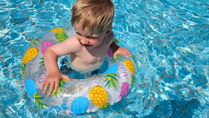 Sweet, blond boy swimming with a pineapple swim ring. Summer pool time. Childhood memories. High quality photo