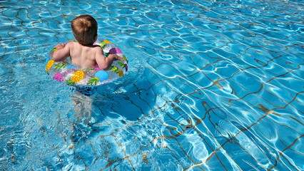 Rear view of blond baby swimming in pool. Pineapple swim ring. Summer vibes and carefree vacation ....