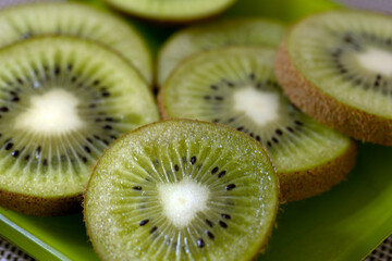 Sliced kiwi fruit arranged on a green plate. The vibrant green flesh is dotted with small black...
