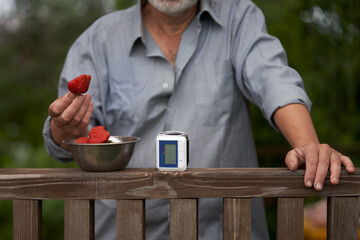 Fragment of an adult man on the terrace of a country house with a strawberry in his hand. In front...