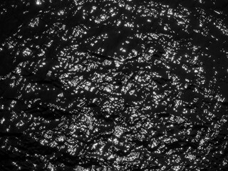 Water surface high contrast top view. Sun glare on water black and white edit. Background abstracted wallpaper texture
