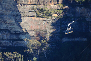 Cable car traverses rugged cliffs with lush trees in a stunning landscape.