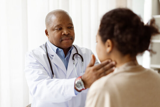 African American doctor man checking lymph nodes of young patient woman during appointment in clinic, therapist man carefully examining the neck and throat area, closeup