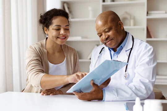 Happy African American doctor reviewing medical records with smiling black millennial female patient during visit in modern clinic, therapist man discussing test results with woman, closeup