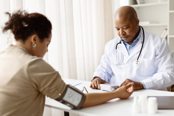 Black Doctor Man Measuring Arterial Blood Pressure Of Female Patient In Clinic, Professional...