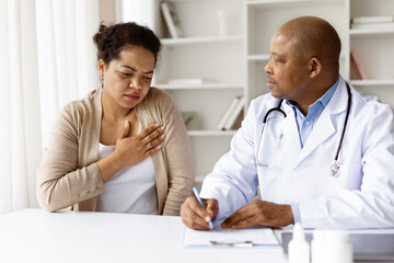 African American male doctor listening carefully to black millennial woman describing chest pain...