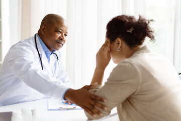 Obraz premium Empathetic African American male doctor comforting black woman experiencing discomfort during clinical consultation, therapist man soothing upset female patient, closeup