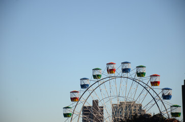 Colorful Ferris wheel with city skyline and clear blue sky in the background.