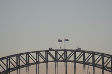 Flags waving atop Sydney Harbour Bridge silhouetted against evening sky