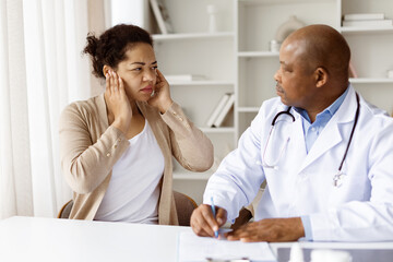 African American male doctor listening carefully to black millennial woman describing ear pain...