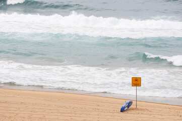 Beach with warning sign, lifeguard gear, and ocean waves crashing ashore