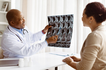 Smiling African American male doctor in medical coat explaining spine x-ray results to attentive...