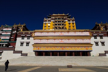 Front view of Gomang Monastery near Ngawa in the Amdo region, featuring vibrant Tibetan architecture, intricate details, and a lone figure walking across the expansive courtyard.