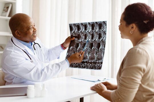 Smiling African American male doctor in medical coat explaining spine x-ray results to attentive black female millennial patient during appointment in modern clinic, closeup - Powered by Adobe