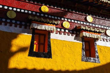 Traditional Tibetan windows with decorative frames on the vivid yellow wall of Taktsang Lhamo Monastery in Langmusi, a spiritual site in the Amdo region of Greater Tibet.