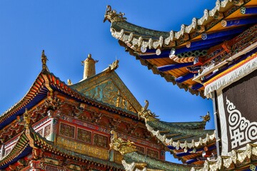 Intricate Tibetan architecture details of Taktsang Lhamo Monastery (Langmusi), a sacred Buddhist site in the Amdo region, showcasing vibrant ornamentation and traditional roof design.