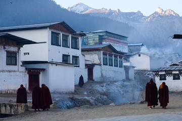 Buddhist monks walk through smoky alleys of Taktsang Lhamo Monastery in Langmusi, a serene Tibetan town nestled in the Amdo region, surrounded by misty mountains.