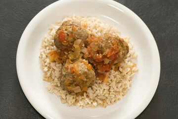 Top view of a plate with rice and three meatballs.