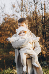 Fototapeta premium Happy father hugging cute baby son in autumn field in soft evening light. Parenthood. Portrait of dad and little child in cozy stylish clothes embracing in fall park