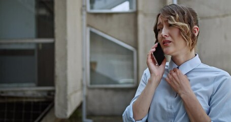 Stressed young woman on phone call expressing worry or anxiety, possibly after a car accident. She gestures with her hands while standing near parked cars in an urban setting. - Powered by Adobe