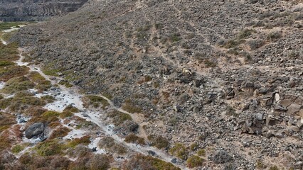 volcanic arid landscapes with trils, cliffs, and scattedred vegetation.