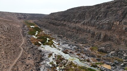 volcanic arid landscapes with trils, cliffs, and scattedred vegetation.