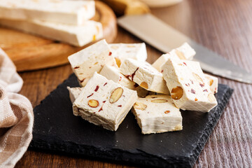 White nougat bars with almonds and dried fruit on cutting board on wooden table.