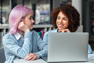 Smiling diverse young women collaborating on laptop in modern coworking space. Concept of teamwork, digital nomads, freelance, generation Z and creative business