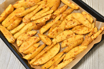 Country-style potatoes - wedges with skins in spices on a baking sheet. Raw