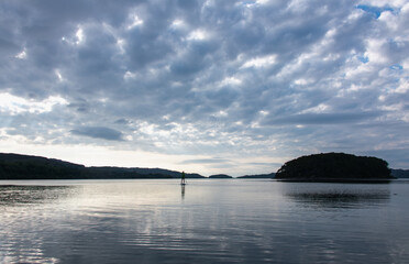 A paddleboarder on a Scottish sea loch under a moody, cloudy and grey sky.