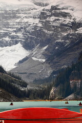 Iconic red canoes, both docked and paddling through Lake Louise emerald-turquoise waters, with...