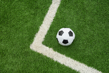 Soccer ball on green grass field with corner. Football stadium background. View from above.