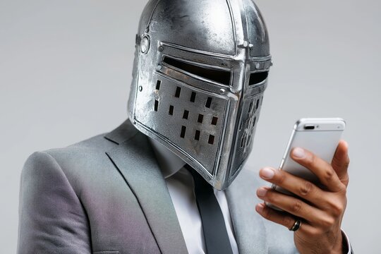 Man in business suit wearing medieval knight helmet while using smartphone, symbolizing digital security, anonymity, and corporate protection concept