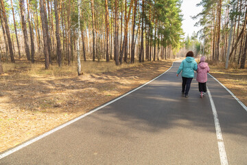 Little girl riding scooter while walking with her grandmother in the forest on a sunny day