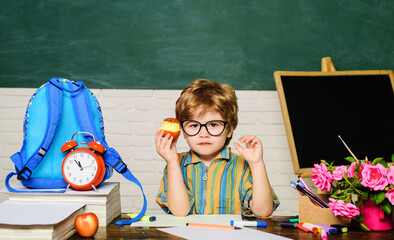 Lunch time. Cute serious schoolboy sitting at table and eating apple in classroom. School break....