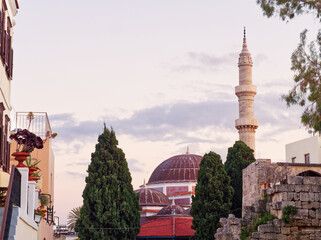 Ottoman-style mosque with dome and tall minaret, surrounded by cypress trees and old buildings in Rhodes island old town