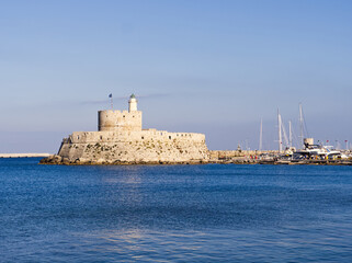 Rhodes island fortress with lighthouse and modern yachts inside the harbor with calm blue waters. Greece