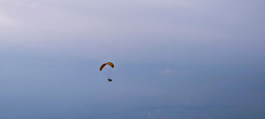 A person engaged in powered paragliding, also known as paramotoring. This activity involves a person wearing a motor and a paraglider wing, allowing them to take off and fly.