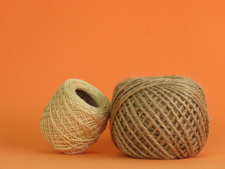 Roll of thick ecru sewing thread and roll of jute rope on orange background.
