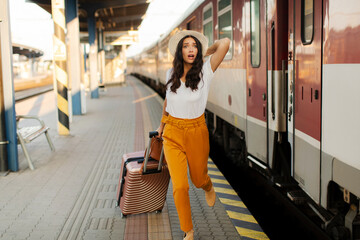 Woman running and chasing the leaving train at railway station platform, waving hand and rushing to...