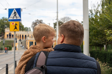 Dad holding little boy in arms while walking through the city on a chilly day. Concept of fatherhood, emotional connection, street life with kids and everyday family experience in urban environment.