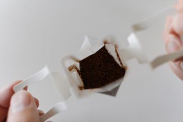 Close-up top view of male hands carefully placing drip coffee bag into transparent glass cup,...