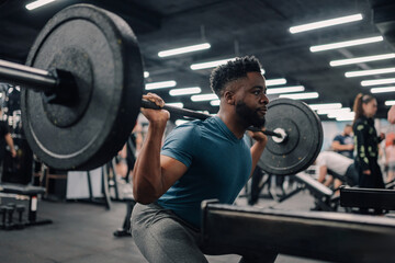 Determined athlete performing squats with heavy barbell in gym