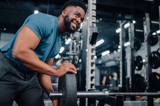 Muscular bodybuilder adding weights to barbell in modern gym