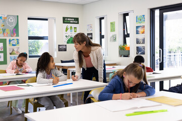 In school, female teacher helping diverse students with assignments, fostering learning