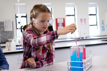 Girl in school lab conducting experiment with test tubes, wearing safety goggles