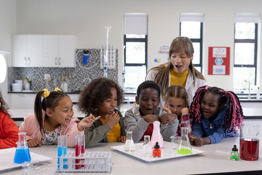 Diverse children in science class observing colorful chemical reactions in beakers, at school