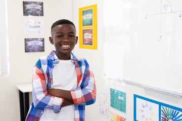 Confident african american boy smiling in classroom, standing by whiteboard with equation, at school